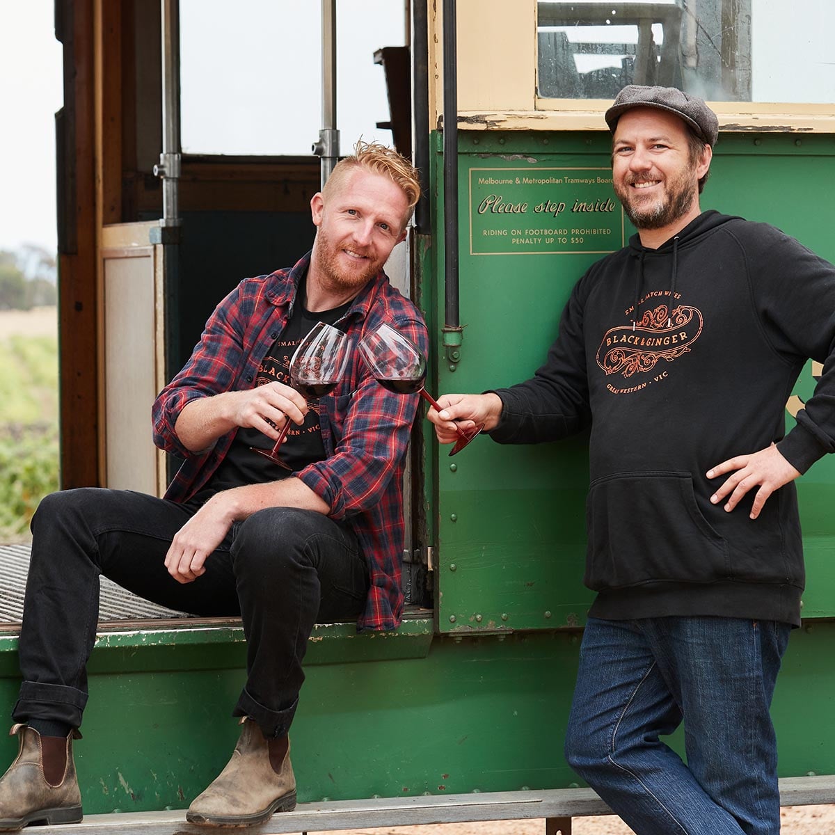 Darcy and Hadyn cheers with glass in hand in front of tram at Hounds Run Vineyard