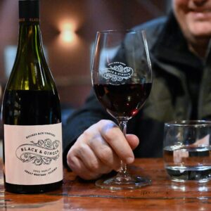 A bottle of the Virginia Merlot on the bar next to customer holding a glass of merlot