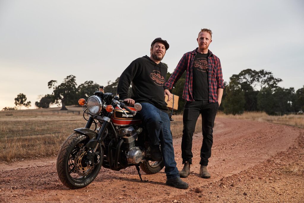 Hadyn Black & Darcy Naunton pose with a vintage motorbike on a gravel driveway