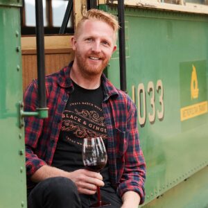 Darcy Naunton sitting on the side of a W Class Tram at Hounds Run with a glass of wine in hand