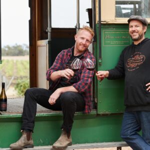 Hadyn and Darcy cheers in front of a vintage tram at Hounds Run Vineyard
